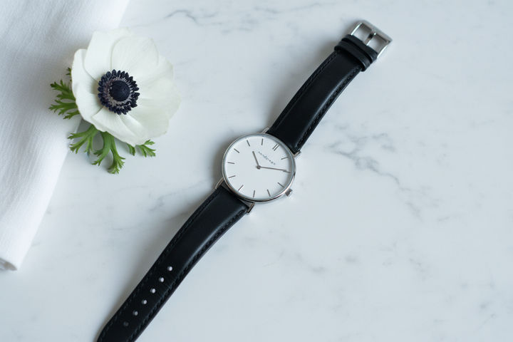 Nordgreen Native 32mm Silver Case Black Leather watch flat lay on white marble with white anemone